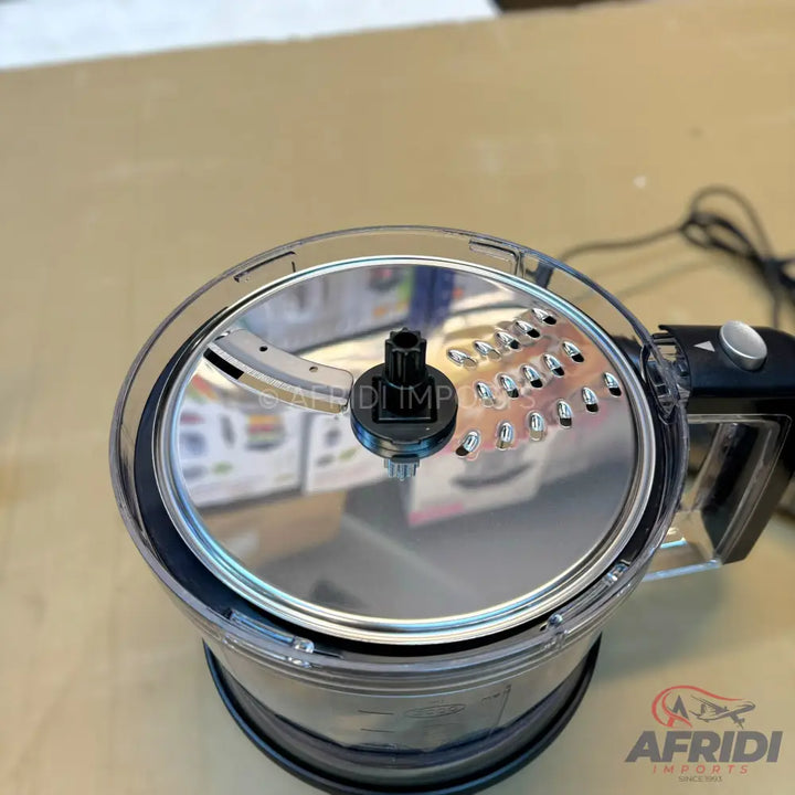 Food processor with a clear bowl and a stainless steel grating/slicing disc.