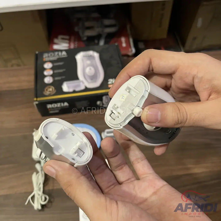 A person demonstrating the open battery compartments of two white and gray handheld electric shavers.