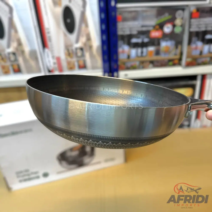A shiny metal wok with a decorative etched band on its exterior bottom.