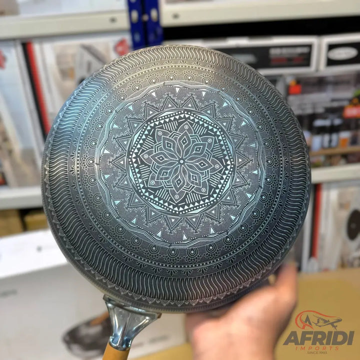A dark-colored frying pan with an intricately etched mandala design on its underside.