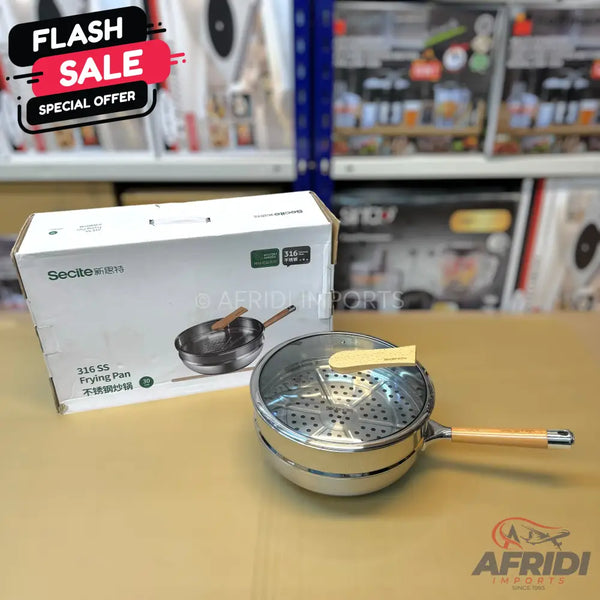 A stainless steel frying pan with a wooden handle and a glass lid, packaged in a box, featuring a steaming rack insert.