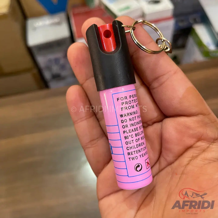 Pink personal defense spray with a black cap and red nozzle, attached to a keyring.
