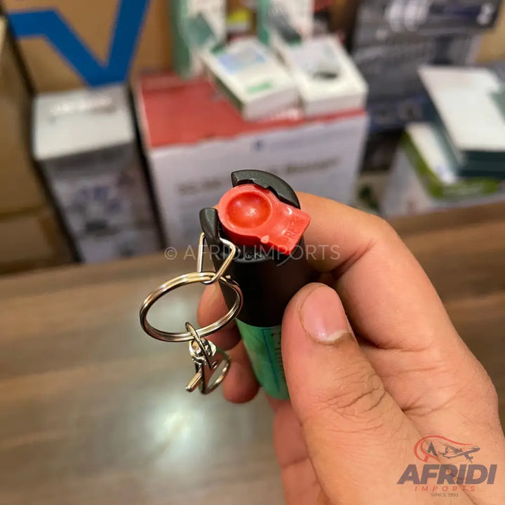 A black and green pepper spray keychain with an orange nozzle.