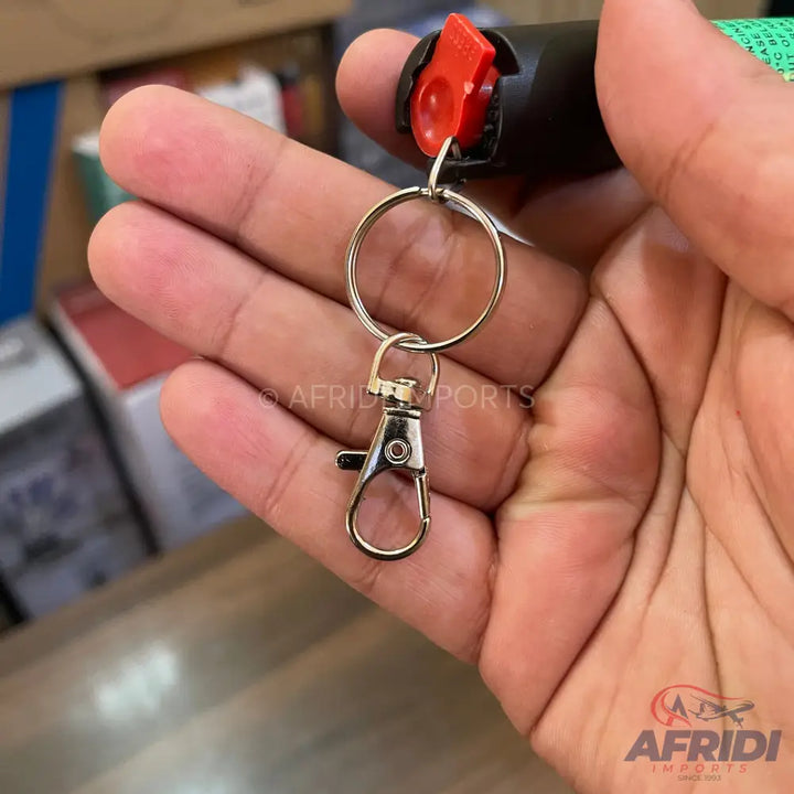 A black pepper spray canister with a red safety lock and a keyring attachment.