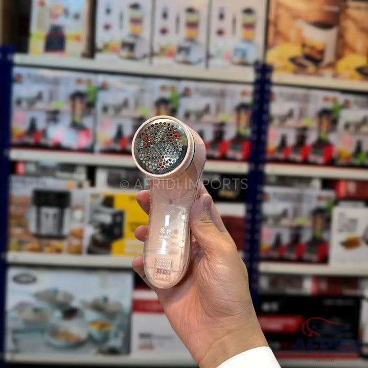 A handheld electric lint remover with a rose gold finish and a perforated metal cap.