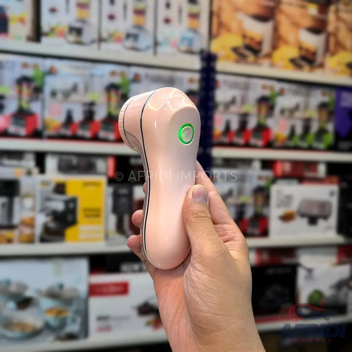 A handheld, pale pink electric lint remover with a green indicator light.