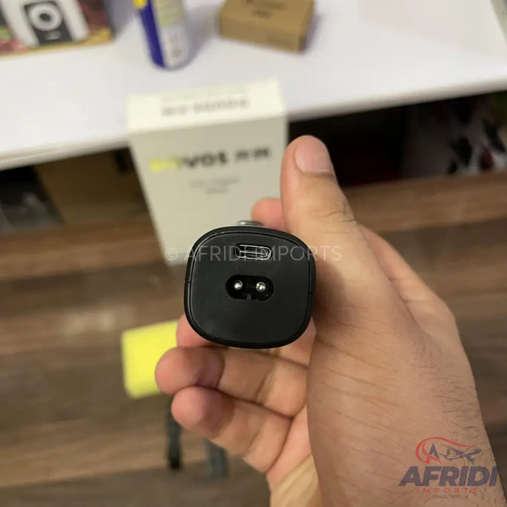 Black electronic device with a two-prong connector and a USB-C port, held in a hand.