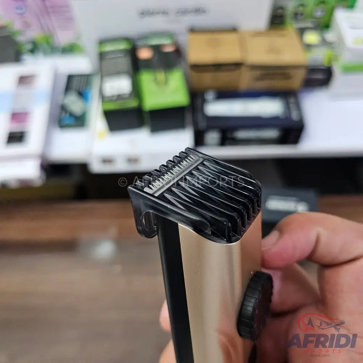 Gold and black electric hair trimmer with a clear plastic comb attachment.