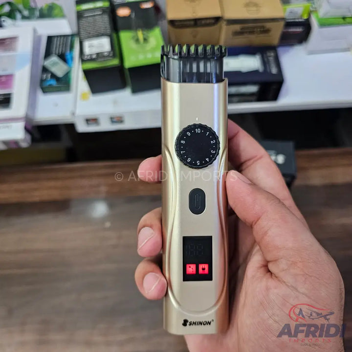 A gold-colored electric hair clipper with an adjustable dial for length settings and a digital display.