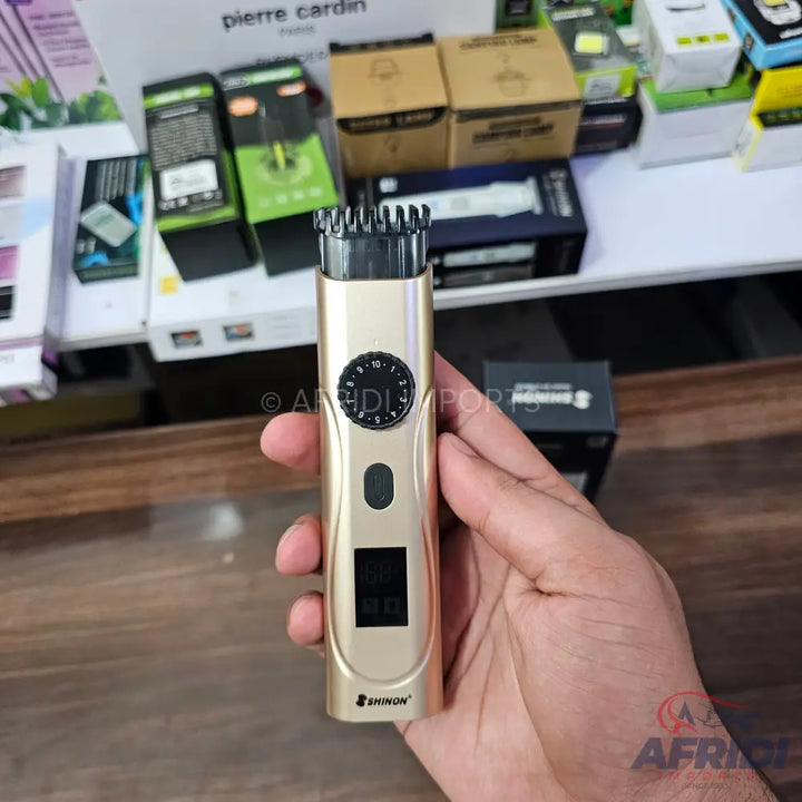 A gold-colored electric beard trimmer with an adjustable dial, an on/off switch, and a digital display.