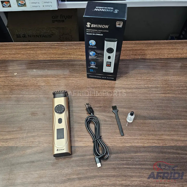 A gold rechargeable hair clipper with an LCD display and adjustable cutting length settings, packaged with a USB charging cable, cleaning brush, and lubricating oil.