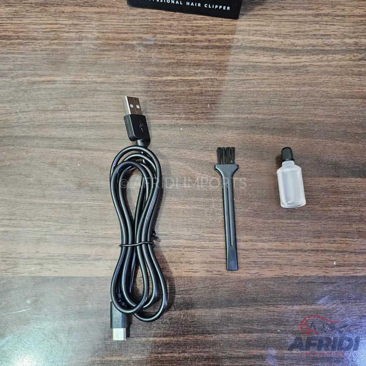 Black USB-A to USB-C charging cable, cleaning brush, and oil bottle for a hair clipper.