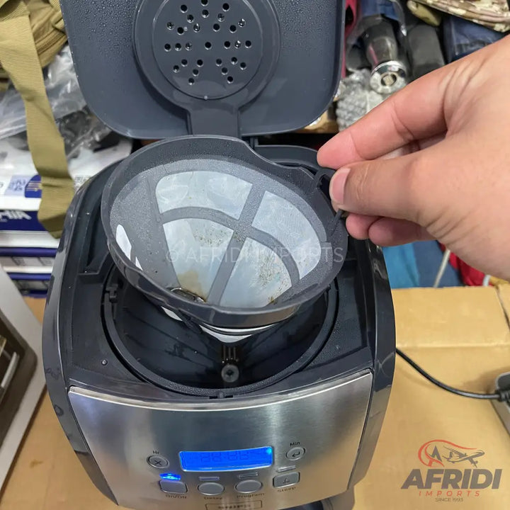 A black and silver coffee maker with an open lid, showing a removable mesh filter and a blue illuminated display.