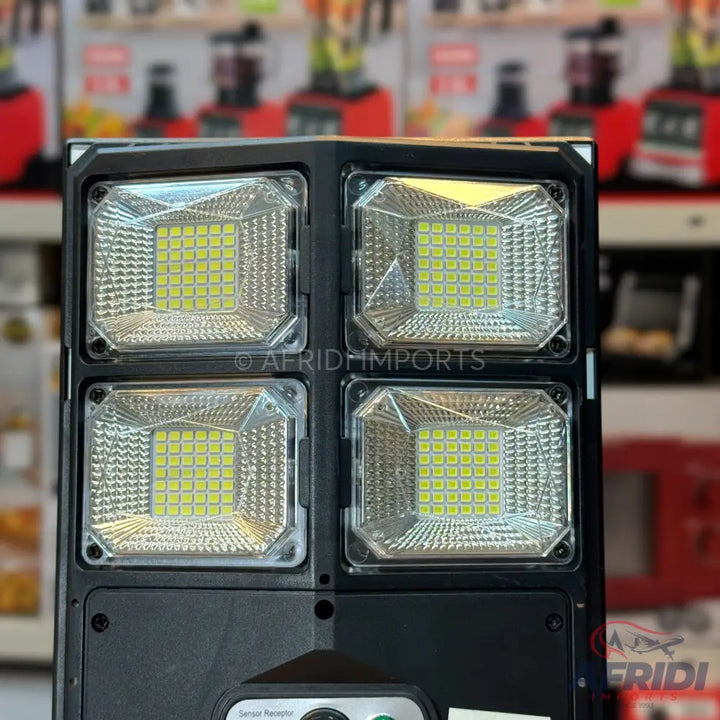 A black rectangular solar-powered LED floodlight with four distinct light panels, each containing multiple small, square-shaped LED bulbs.