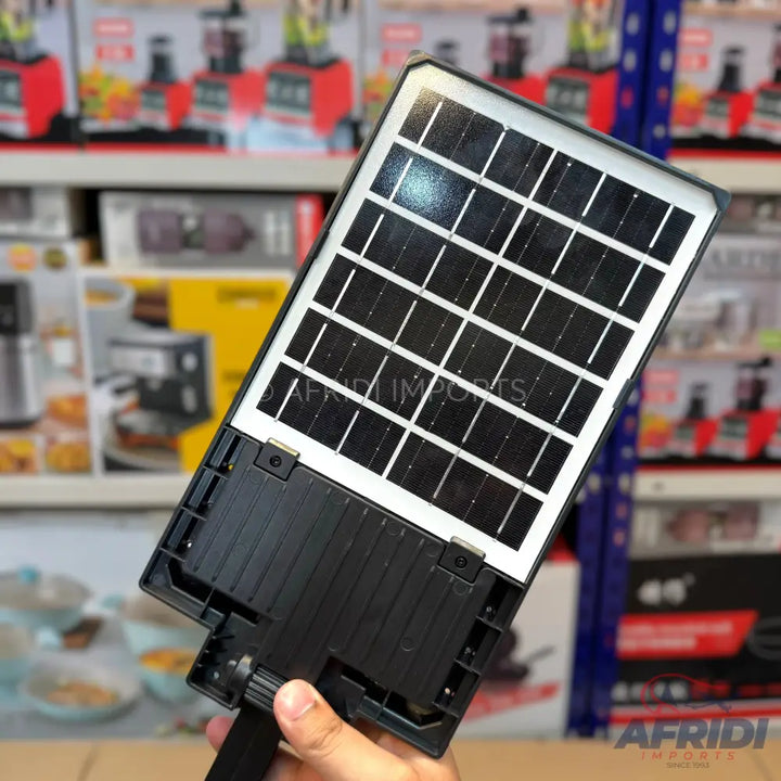 A person holding a black solar-powered street light with a grid of solar cells.