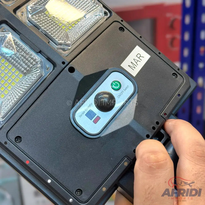 Black rectangular solar-powered security light with multiple LED panels and a control panel featuring an on/off switch and sensor indicators.