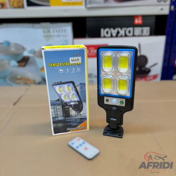 A black solar-powered LED street light with four rectangular light panels and a remote control.