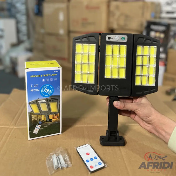 A black, three-panel, solar-powered sensor street lamp with bright LED lights, accompanied by its packaging, mounting hardware, and a remote control.