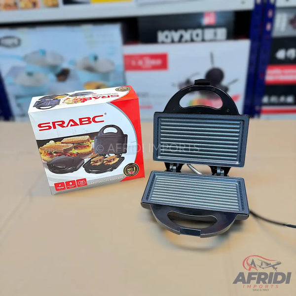 An open, black electric grill or sandwich maker with ribbed cooking plates, accompanied by its packaging box.