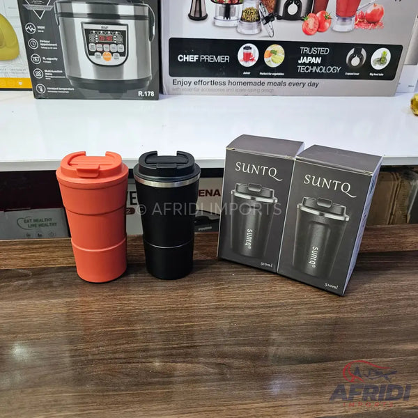 Two insulated travel mugs, one orange and one black, next to two boxes for a black travel mug.