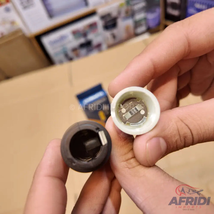 Two cylindrical objects, one black and one white, held in hands, with the white one revealing a battery compartment and metal contacts inside.