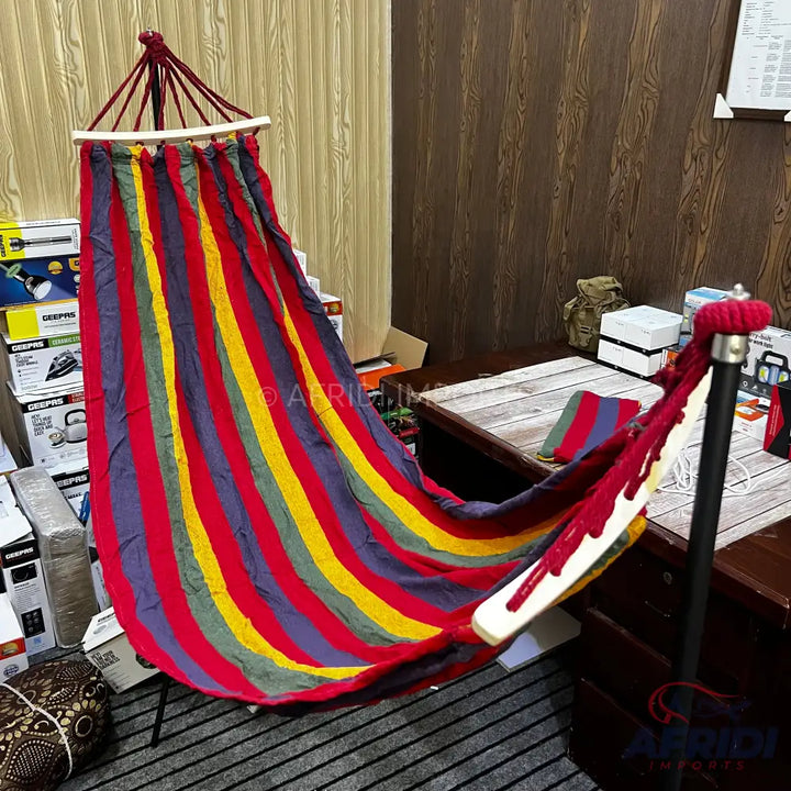 A colorful striped fabric hammock with a wooden spreader bar.