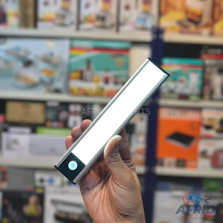 A hand holding a sleek, silver LED light bar with a circular button on one end.