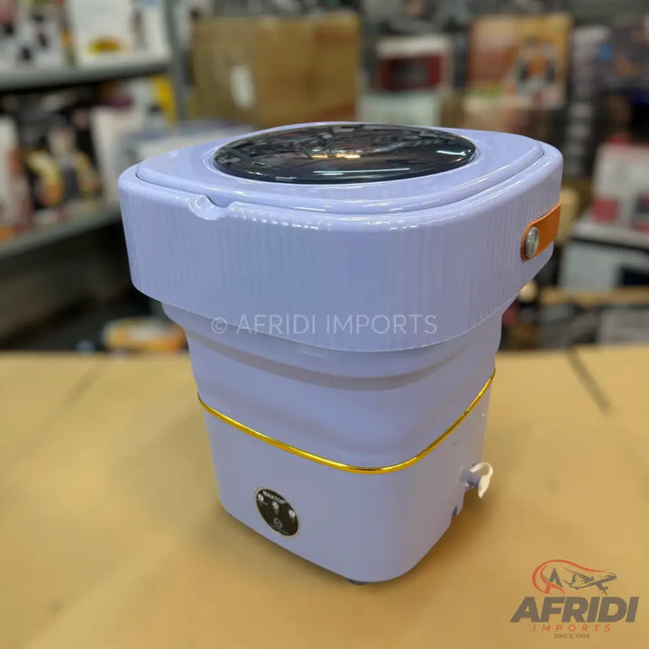 A light purple, foldable, portable washing machine with a dark circular lid and gold trim.