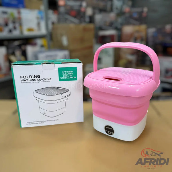 A pink and white portable folding washing machine with a handle, next to its packaging box.