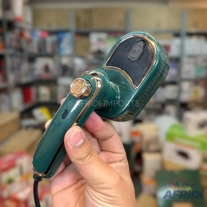 A handheld, dark green, and gold-trimmed portable garment steamer with a cord.