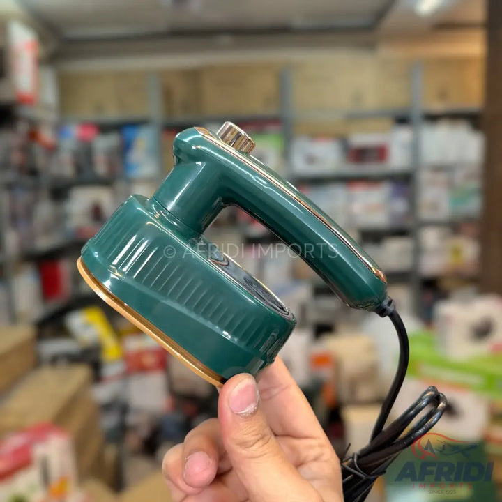 A person holding a dark green handheld steam iron with a gold base and black power cord.