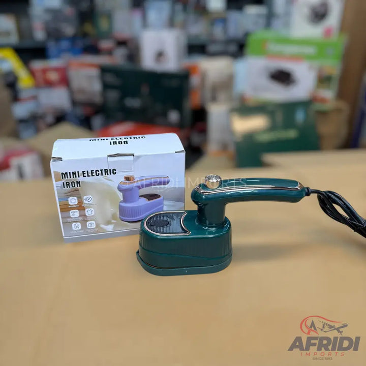 Dark green mini electric iron with a matching stand, a gold-colored knob, and a black power cord.