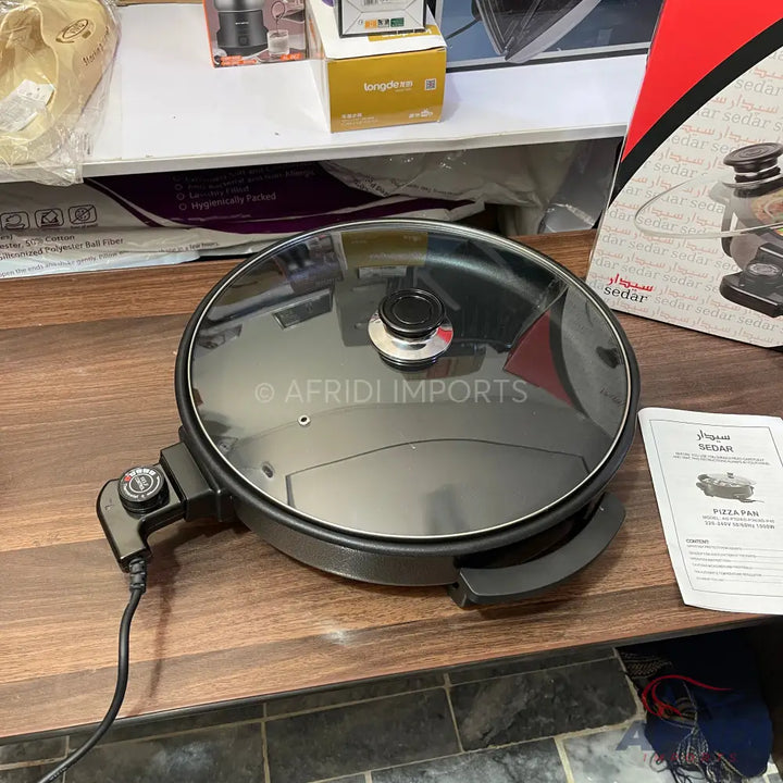 Black electric pizza pan with a glass lid and temperature control.
