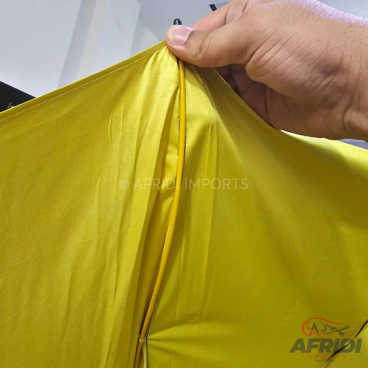 A yellow fabric, possibly part of an umbrella or tent, with a visible seam and a hand holding the edge.