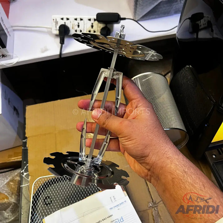 A clear rotisserie spit with four metal prongs and two round, gear-like discs.