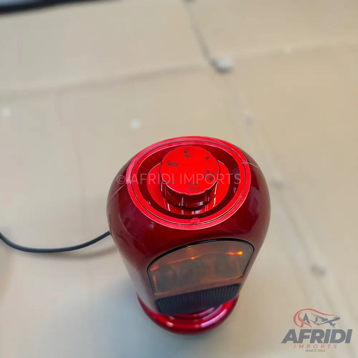 A shiny, dark red car gear shift knob with a transparent top and an illuminated display.