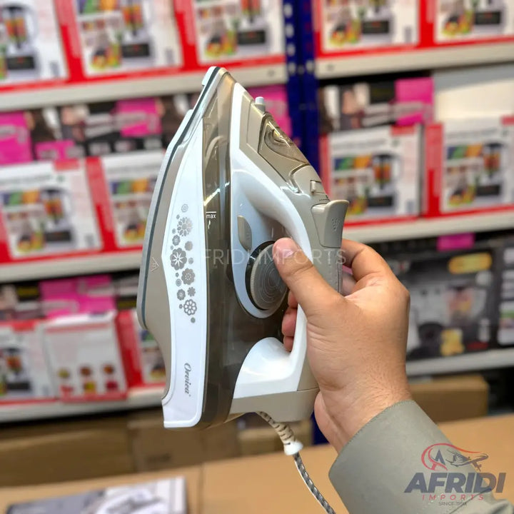 A human hand holding a grey and white steam iron with a floral pattern on its side.