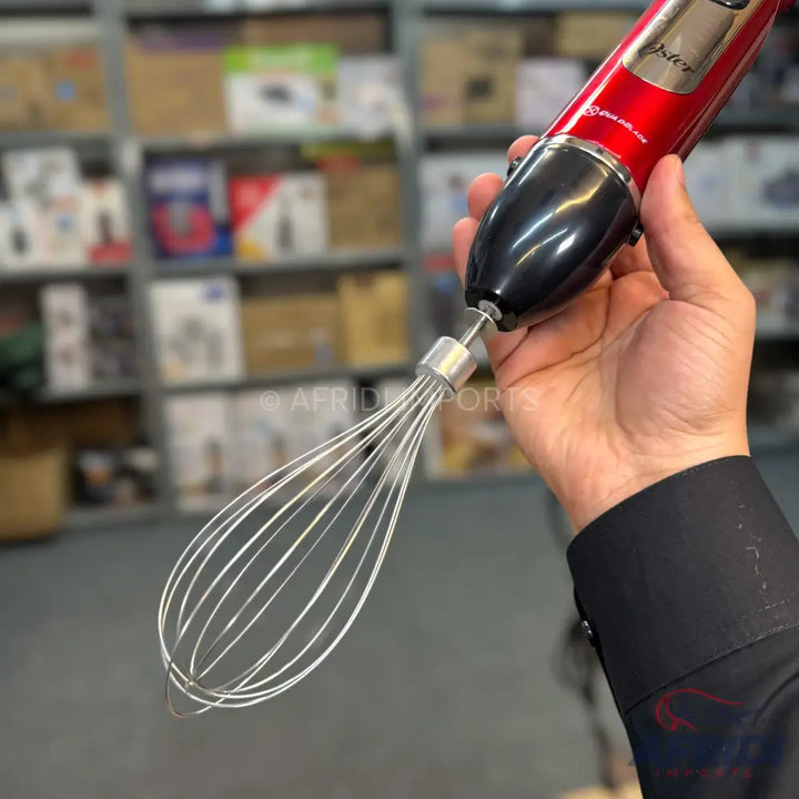Red and black handheld immersion blender with a whisk attachment.