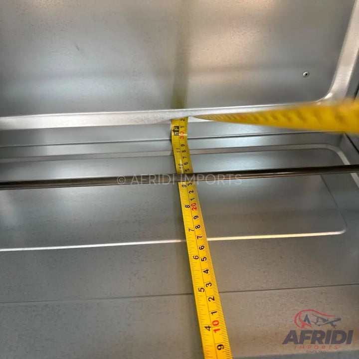 An interior view of a metal oven with a measuring tape showing the depth.