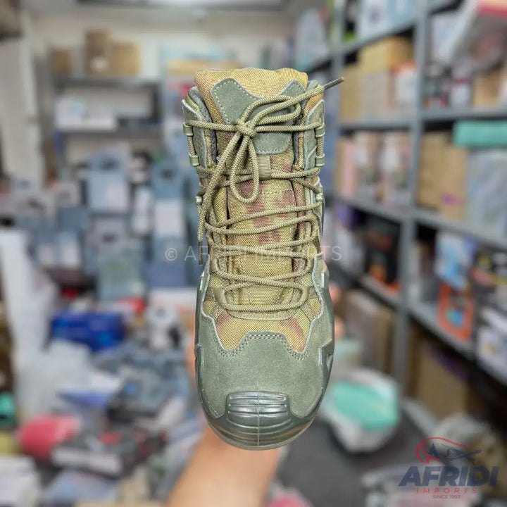 An olive green and camouflage patterned hiking boot with thick laces.