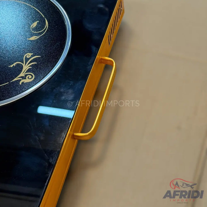 Black induction cooktop with a single burner, gold decorative accents, and a gold handle.