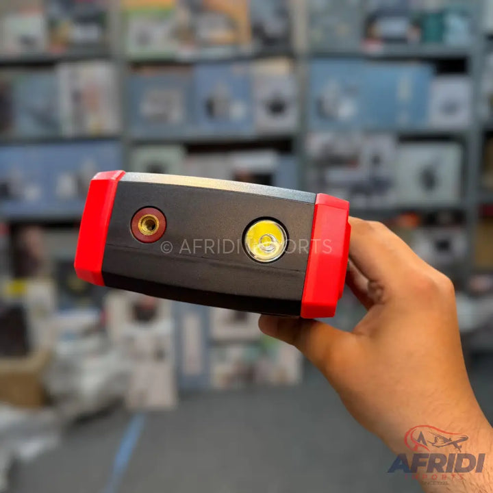 A compact, black and red portable jump starter with two circular ports, one gold and one silver, on its top surface.