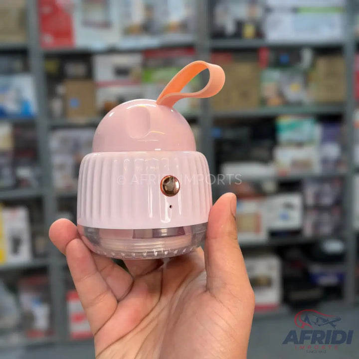 A handheld, pink and clear, rechargeable lint remover with a ribbed base and a carrying strap.
