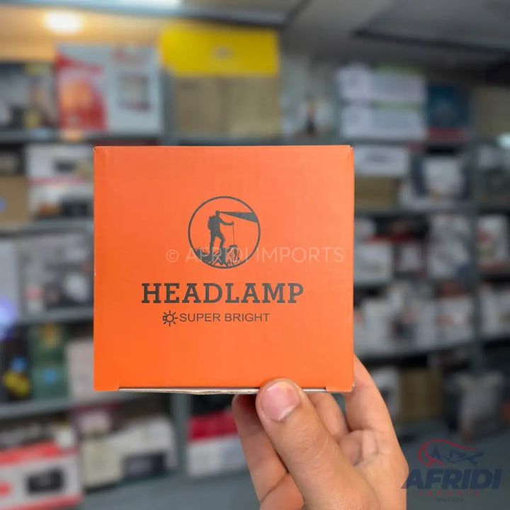 Orange box with a logo of a person climbing a mountain, labeled ’HEADLAMP SUPER BRIGHT’.