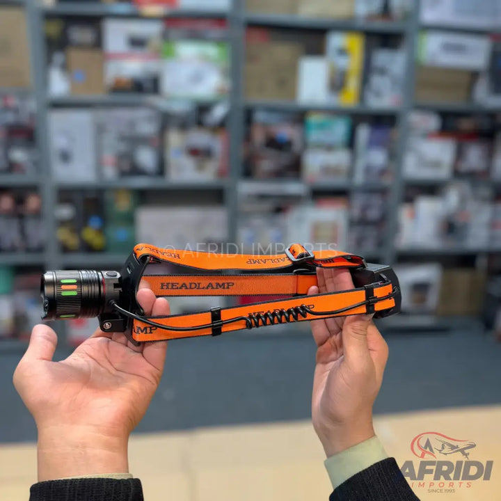 An orange headlamp with a black elastic strap and a metallic, cylindrical flashlight unit on the front.