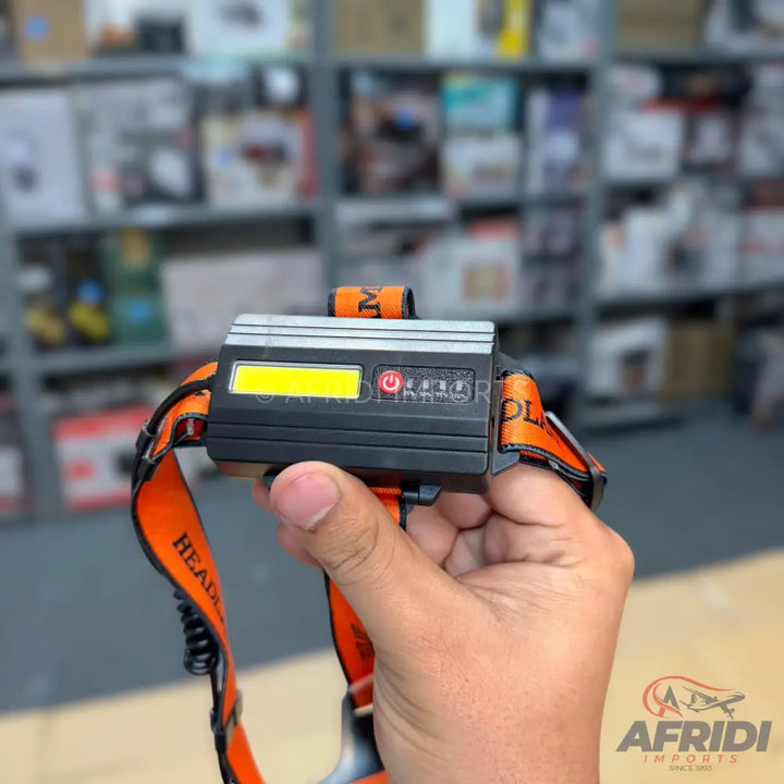 Black and silver headlamp with an orange elastic strap.