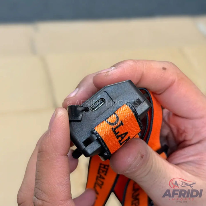 Black headlamp with an orange elastic strap and a USB-C charging port.