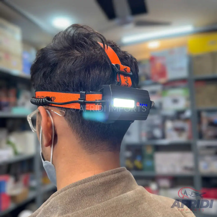 Person wearing an orange and black headlamp with a bright white light.