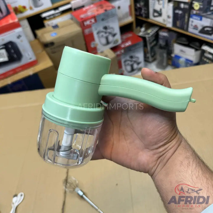 A handheld, light green electric food chopper with a clear container and stainless steel blades.