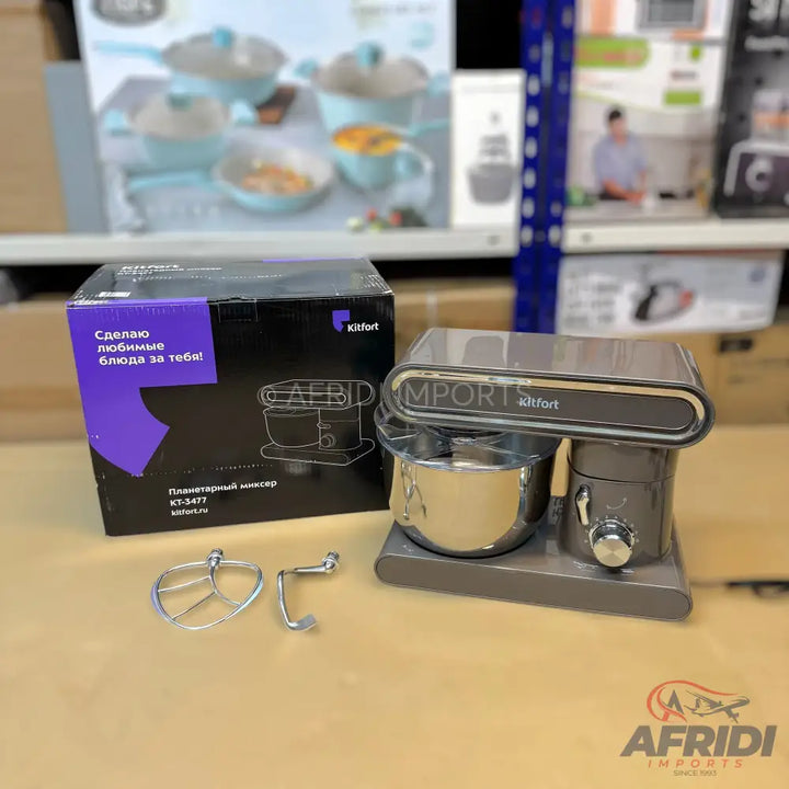 A boxed Kitfort planetary mixer with a dark grey finish and a stainless steel bowl, accompanied by two mixer attachments.